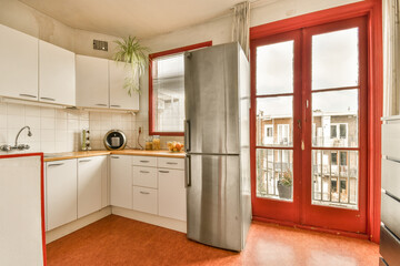 a kitchen with red walls and white cupboards on the door to the left is an open window that looks out onto the street