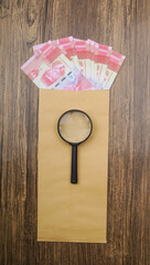 Rupiah money in envelope with magnifying glass are lying on wooden table