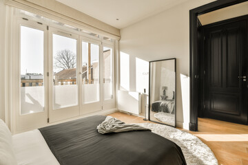 a bedroom with a black bed and white sheets on the floor, in front of a large sliding glass door