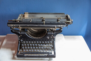 Antique Black Manual Typewriter on a White Desk Against a Blue Wall
