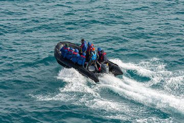 Obraz premium Tourists and Expedition Leader on a Pontoon Boat Riding Through the Waves on a Polar Excursion in Antarctica