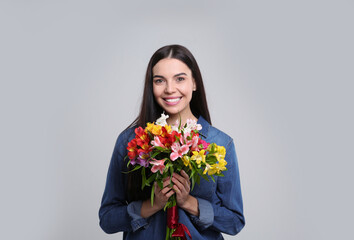 Happy young woman with beautiful bouquet on light grey background