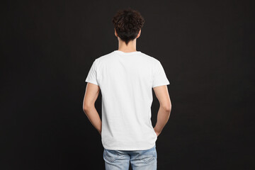 Man wearing white t-shirt on black background, back view. Mockup for design