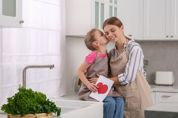 Little daughter congratulating mom with greeting card in kitchen. Happy Mother's Day