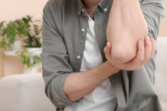 Man suffering from pain in his elbow at home, closeup. Arthritis symptoms