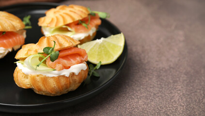 Delicious profiteroles with cream cheese, salmon and cucumber on textured table, closeup. Space for text