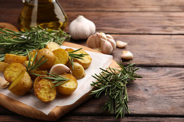Obraz na płótnie Canvas Delicious baked potatoes with rosemary and garlic on wooden board. Space for text