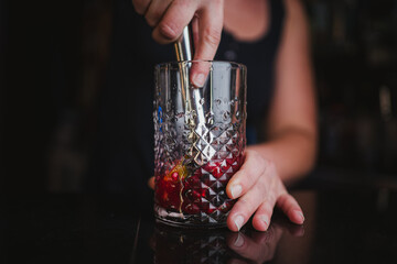 Woman bartender mashing limes and berries using a muddler to make a fruit mojito in a pub bar