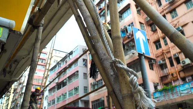 Close-up shot of two workers constructing a bamboo shed with colorful old residential buildings and air conditioners in the background in Shum Shui Po, Hong Kong