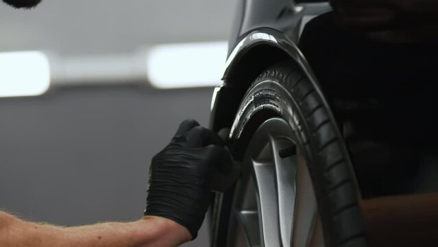 Close up shot of a gloved hand cleaning a black car tire. Repair shop concept. High quality 4k footage