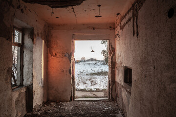 Interior of an abandoned house, heavily damaged, in winter, with a focus on the entrance door and the snow outside, during a freezing afternoon, in Serbia.