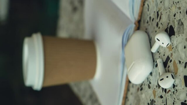Vertical Zoom in out Take away coffee in craft recycling paper cup with paper notebook with wireless headphones. Mockup Coffee break. Audio healing, sound therapy wellness rituals, positive mental