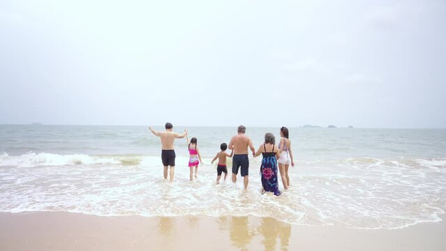 Group of Happy Asian Multi-Generation family in swimwear enjoy and fun outdoor activity lifestyle playing sea water together at tropical island beach during travel ocean on summer holiday vacation.
