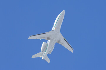 Business Jet overhead.  White private jet flying overhead in under a deep blue cloudless sky. Light twin engine corporate jet aircraft