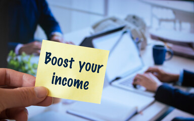 Male hand holding sticky note written Boost your income.