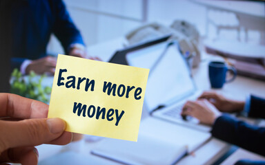 Male hand holding sticky note written Earn more money.