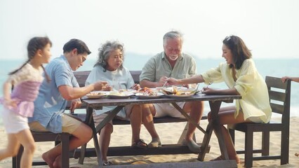 Happy Multi-Generation Asian family having celebration dinner food and drink together at tropical beach restaurant during travel ocean on summer holiday vacation at sunset. Family relationship concept
