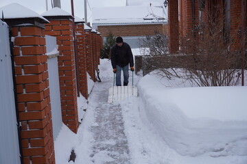 A man cleans snow in the winter in the courtyard of the house.