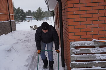 A man cleans snow in the winter in the courtyard of the house.