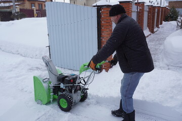 A man cleans snow in the winter in the courtyard of the house,  man cleaning snow with a snow blower