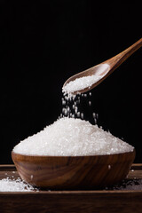 Sugar pours from a wooden spoon on black background