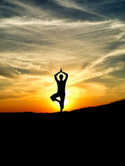 Silhouette young woman practicing yoga on mountain top at amazing sunset.