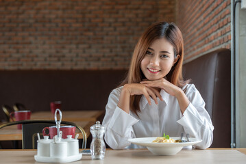 Banner of Woman in white clothes holding and smell white dish plate with pasta homemade spaghetti marinara in restaurant background. Lady smell and eat pasta spaghetti by fork.