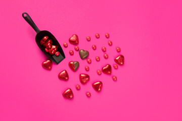 Wrapped and unwrapped heart shape chocolate candies in red foil on pink background