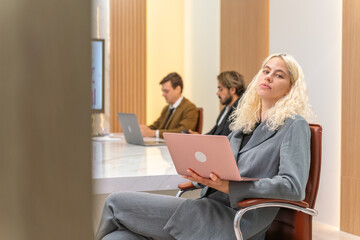 Serious look blonde hair businesswoman with a pink laptop in a meeting room with her team colleague 