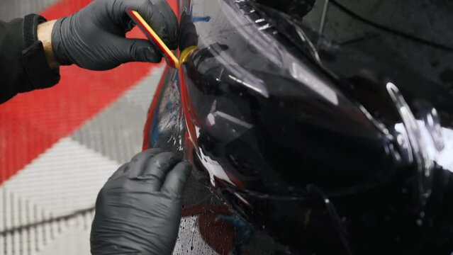 Close shot of a tinting fil being put with a scraper on a car headlight. High quality 4k footage