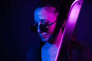 Young woman in a leather jacket in the dark with a machete knife in her hands. Neon light blue pink...