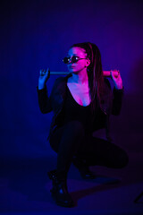 Young woman in a leather jacket in the dark with a machete knife in her hands. Neon light blue pink...