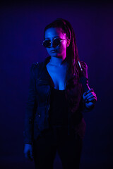 Fototapeta na wymiar Young woman in a leather jacket in the dark with a machete knife in her hands. Neon light blue pink color. Rogue with melee weapons.