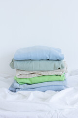 Pile of clothes on white, pastel color palette of stacked sweaters and jeans, fresh clothing folded for ironing