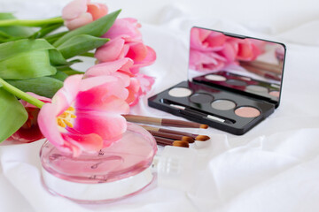 Obraz na płótnie Canvas Pink tulips, eye shadow palette with mirror, brushes and perfume bottle on white background, women makeup cosmetics set