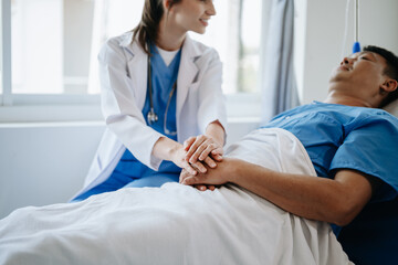 Fototapeta premium Female doctor holding male patient hand on the bed with receiving saline solution in hospital .