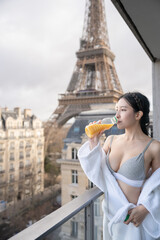 Fototapeta premium Woman drinking orange juice on balcony enjoying view at Eiffel Tower in Paris.