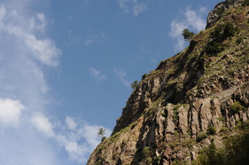 Steep mountain rock slope landscape with green trees an the top peak and blue sky and blue sky