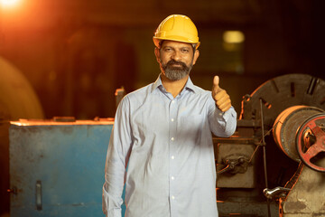 Young indian man engineer wearing safety yellow helmet or hard hat do thumbs pose with hand while...