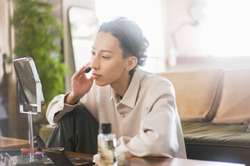 自宅リビングで化粧をしている若いアジア人男性/メンズビューティー