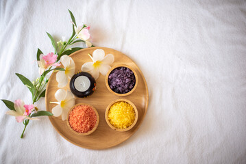 A bowl of orange yellow and purple himalayan salt sat next to a  white plumeria petals perfect for a soothing and luxurious bath.