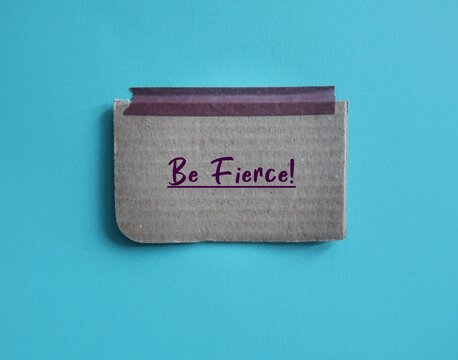 Card box paper stick on blue background with handwritten text BE FIERCE!, concept of affirmation to build self confidence, furiously active or determined - bold strong cool outstanding woman