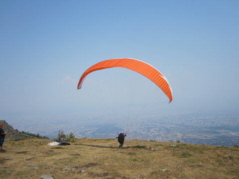 paragliding, orange paraplane, paraglider prepearing to fly on the sky and ground background
