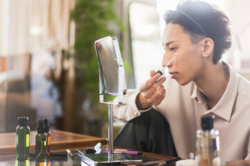 自宅リビングでメイクをしている若い日本人男性のポートレート/コンシーラーでトラブルカバーをしている/メンズビューティー