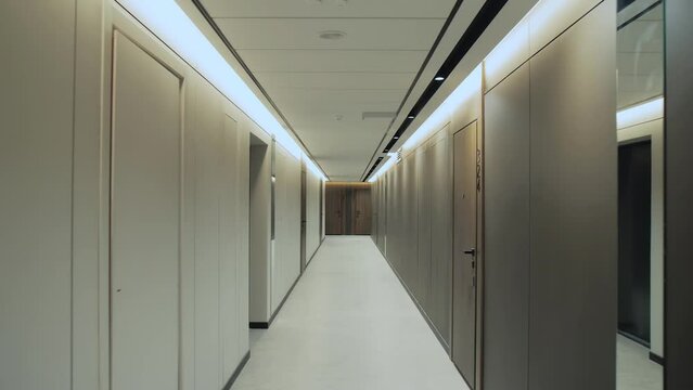 Passage through an empty corridor, empty hall, corridor with closed doors, hidden light, led ceiling, wide shot, slow motion.