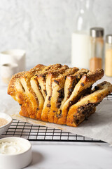 Pull-apart bread with cream cheese, cinnamon, chocolate, prunes, nuts, with streusel on a baking grill. Homemade sweet pastry with ingredients on a light concrete background.
