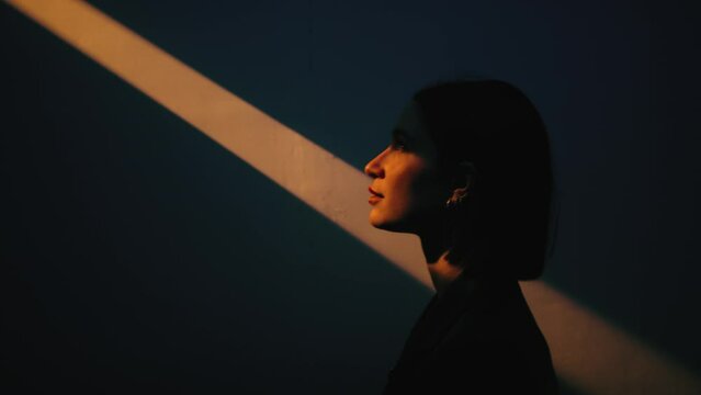 Girl walking on the orange beam light in her face side of the wall