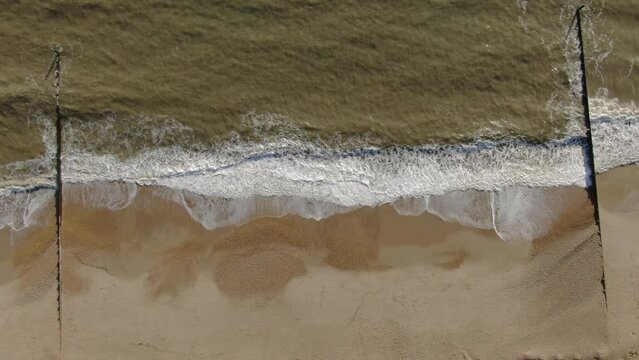 Aerial up motion ooking down peaceful golden colored beach from with waves crashing Bournemouth UK English Channel surf Pacific Ocean