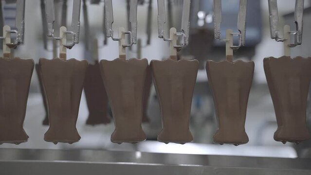 Close up footage of chocolate coated ice cream lollies moving along an industrial food production line, being held upside down by wooden lollipop sticks