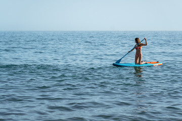 woman on her knees on her surfboard moving through the sea with her oar  